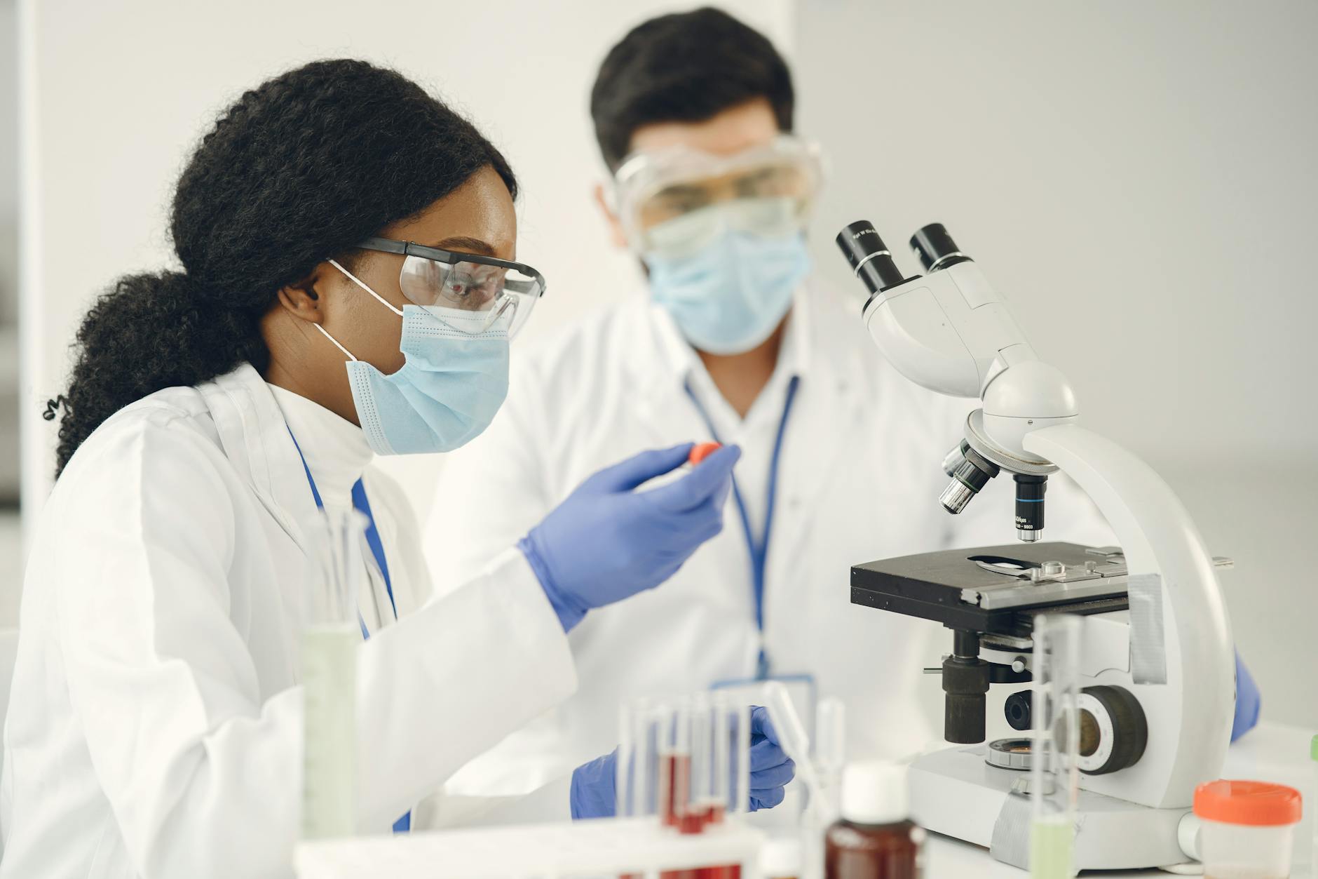 Researchers in protective gear conduct scientific experiments using microscopes in a lab.