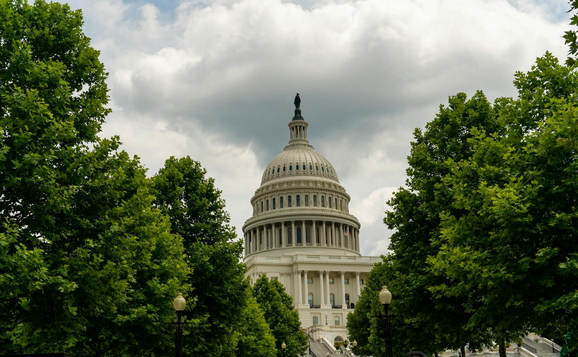 A stunning shot of the Capitol dome surrounded by green trees and cloudy sky in Washington, DC.