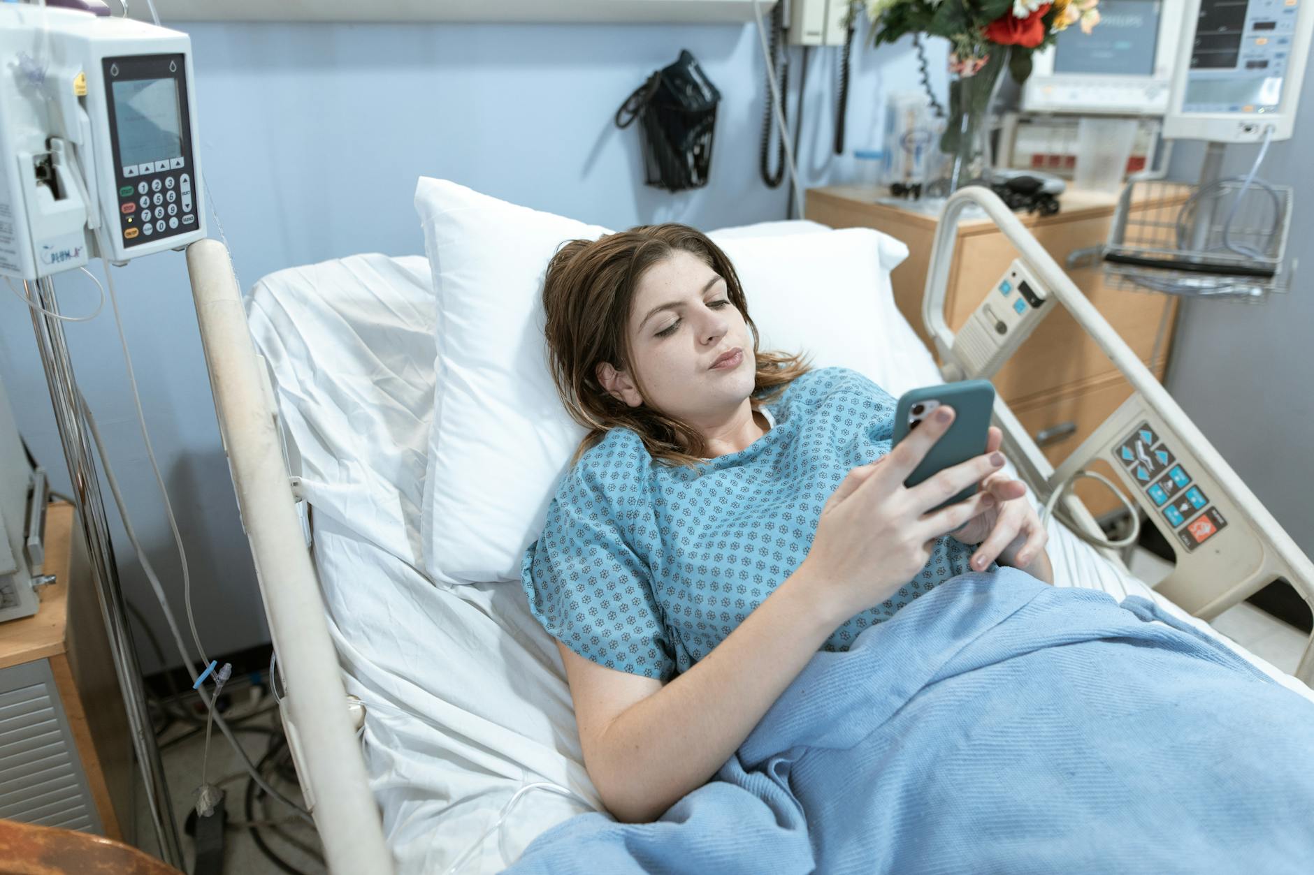 A young woman in a hospital bed using her smartphone while recovering.