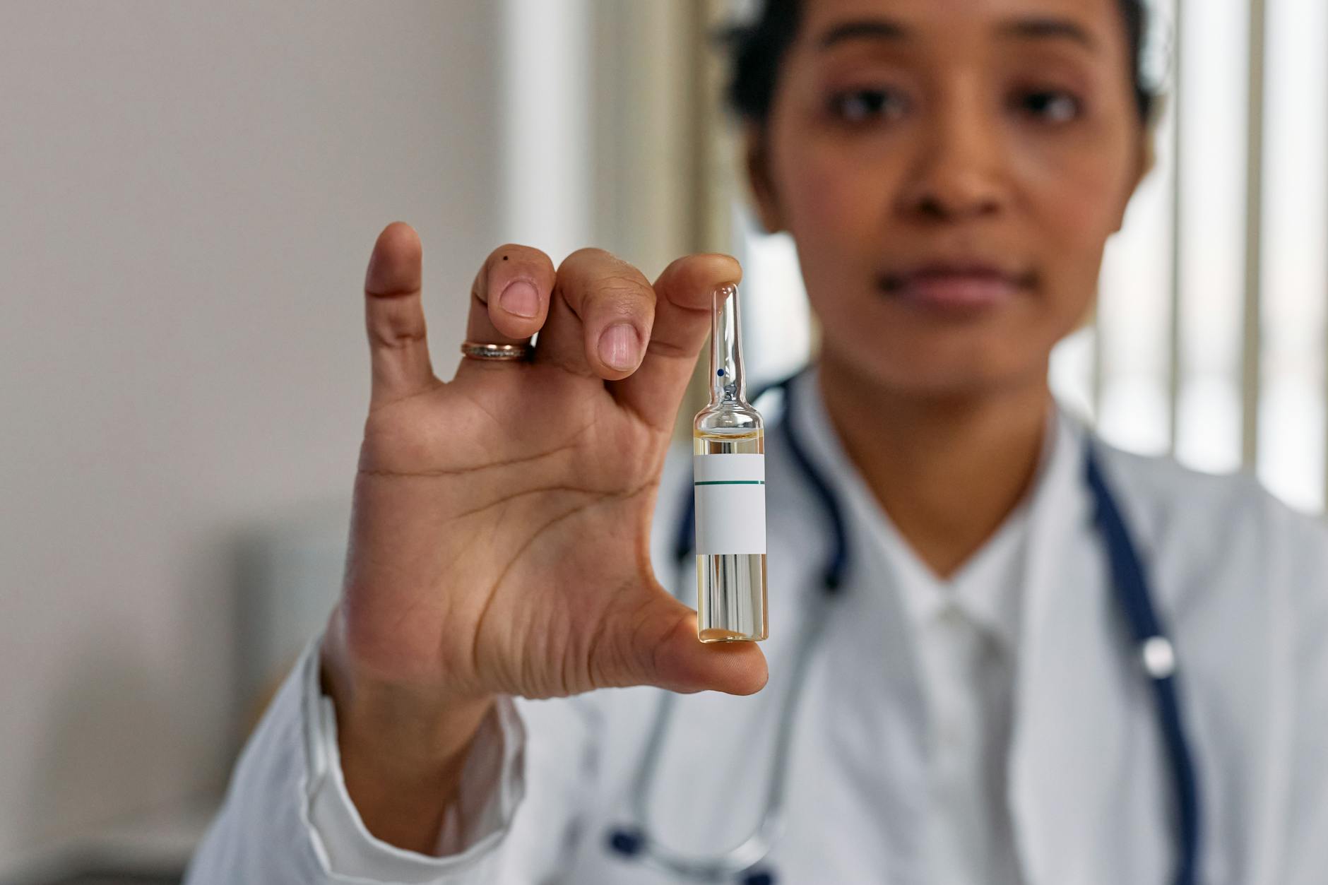 Healthcare professional displaying a vaccine ampoule in a medical clinic for COVID-19 treatment.